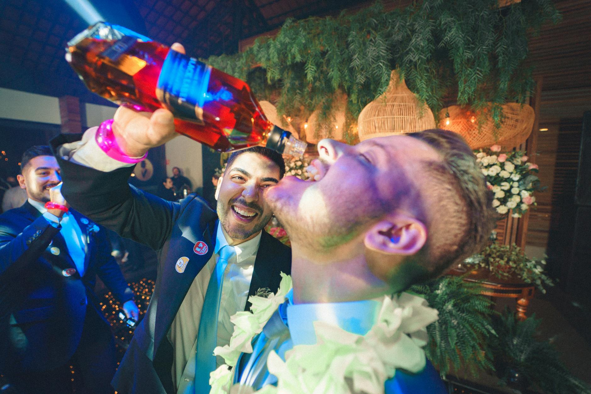 man pouring whiskey from a bottle into another man mouth